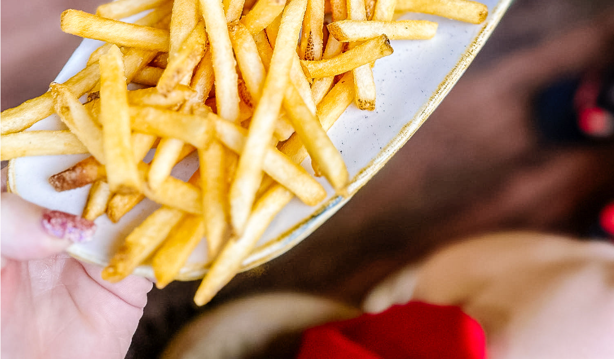 Golden crispy french fries being served on a white plate, close-up shot with soft background blur.