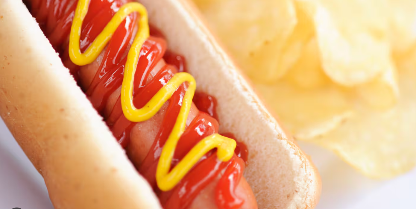 Close-up view of hot dogs with mustard and ketchup condiments arranged in a repeating pattern on a light background.