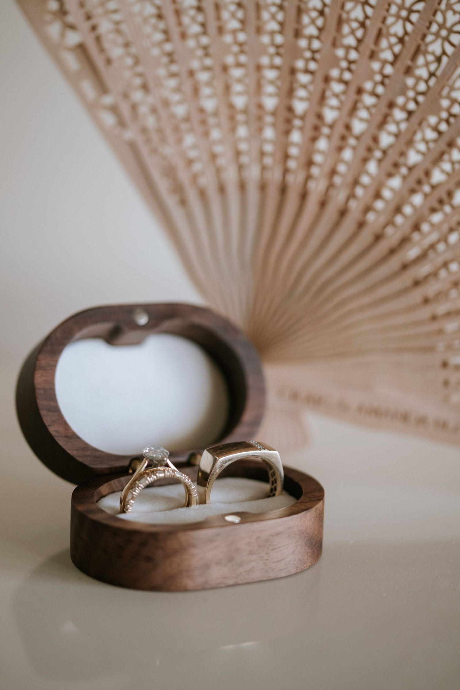 Wedding rings displayed in a wooden heart-shaped box with a decorative fan in the background.