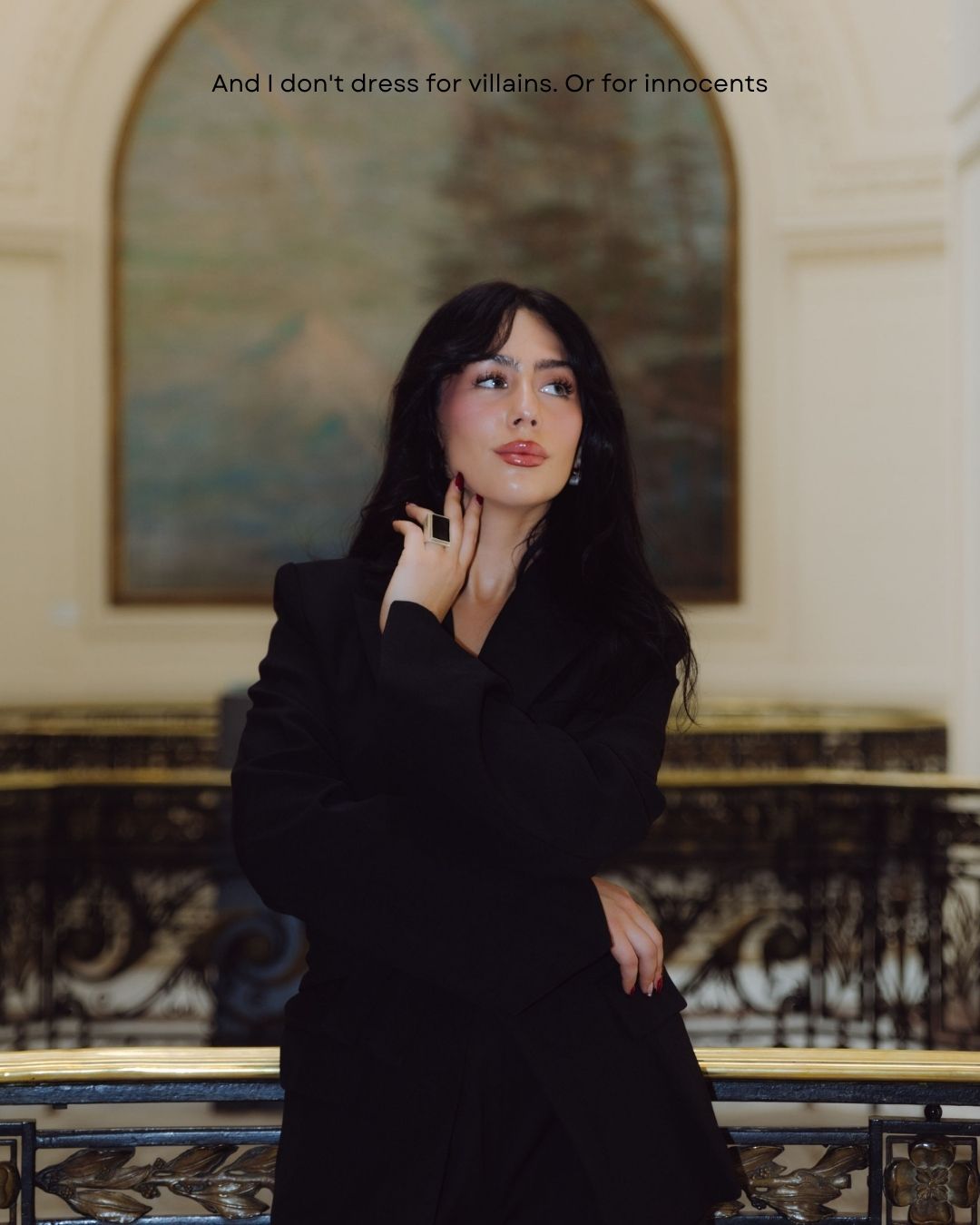 Woman in black blazer posing thoughtfully on elegant staircase with landscape painting background.