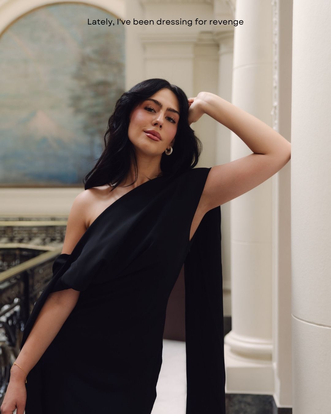 Woman in a black one-shoulder asymmetric gown posing outdoors with a revenge dressing quote.