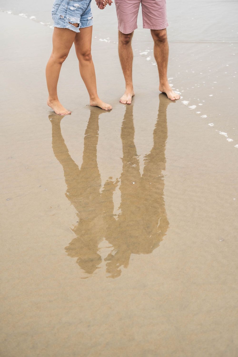 Bare feet and shadows reflected in wet sand on a beach.