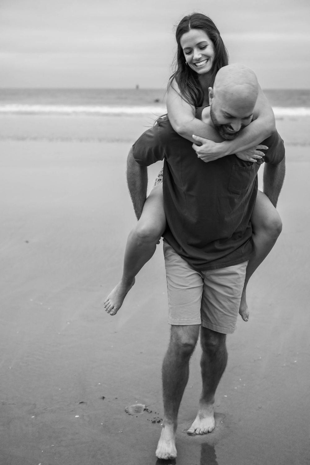 A playful piggyback ride on the beach in black and white.