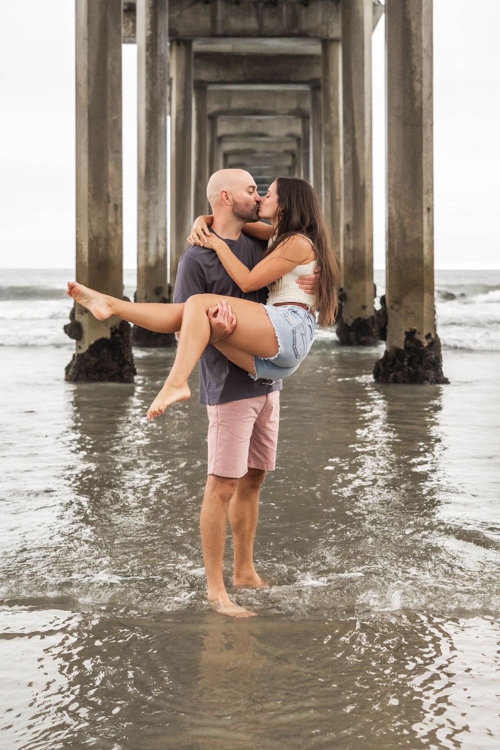 A romantic moment under a pier as waves wash around their feet.