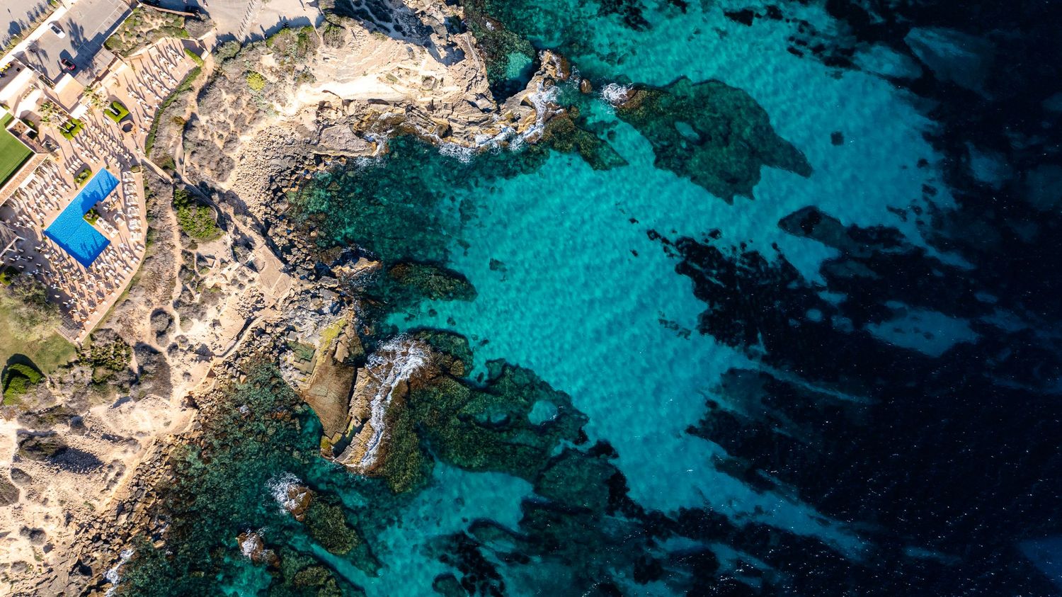 Luxury coastal resort with infinity pool perched on rocky cliffs above turquoise Mediterranean waters.