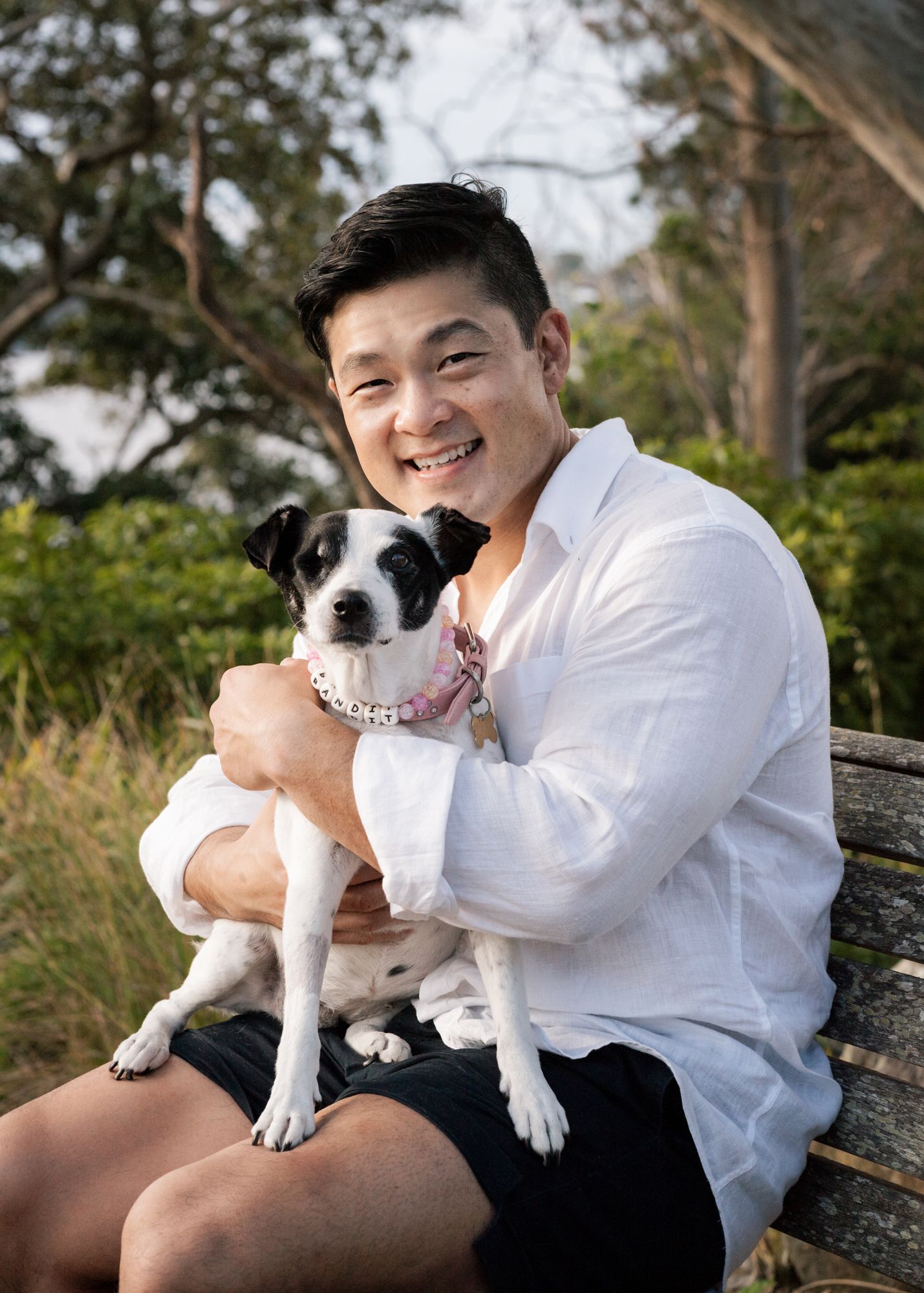 a man smiling while hugging his dog sitting on him and looking towards the camera in Sydney Lilli Pilli Reserve