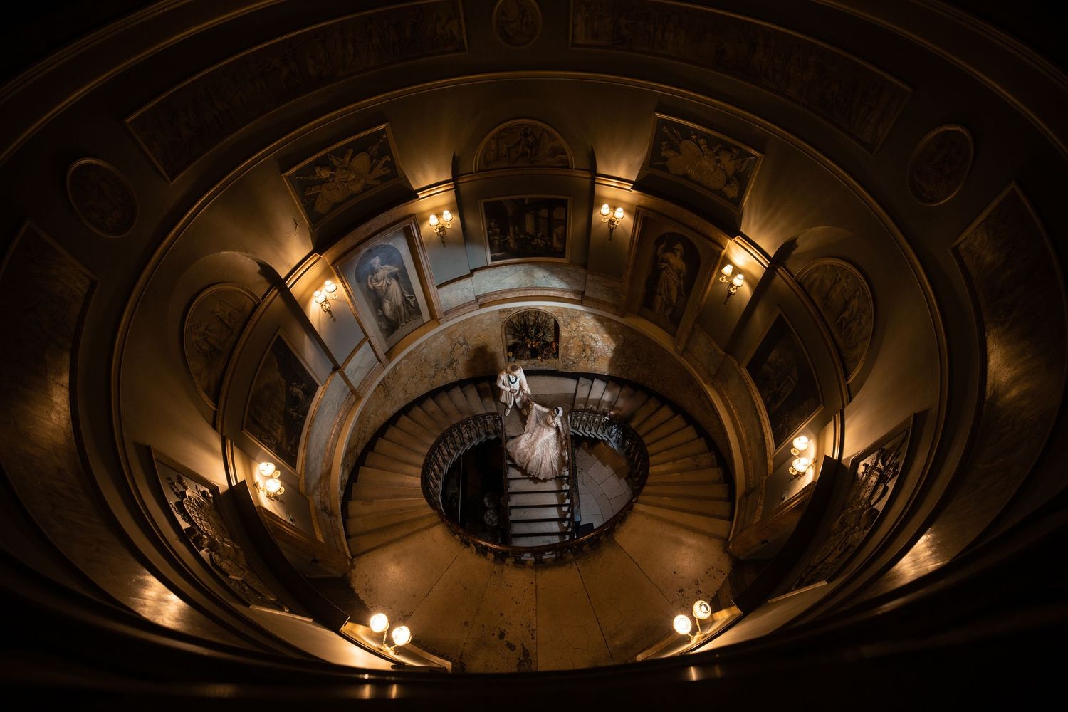 Top-down view of an elegant spiral staircase with warm lighting and ornate architectural details in a historic building. Asian Wedding