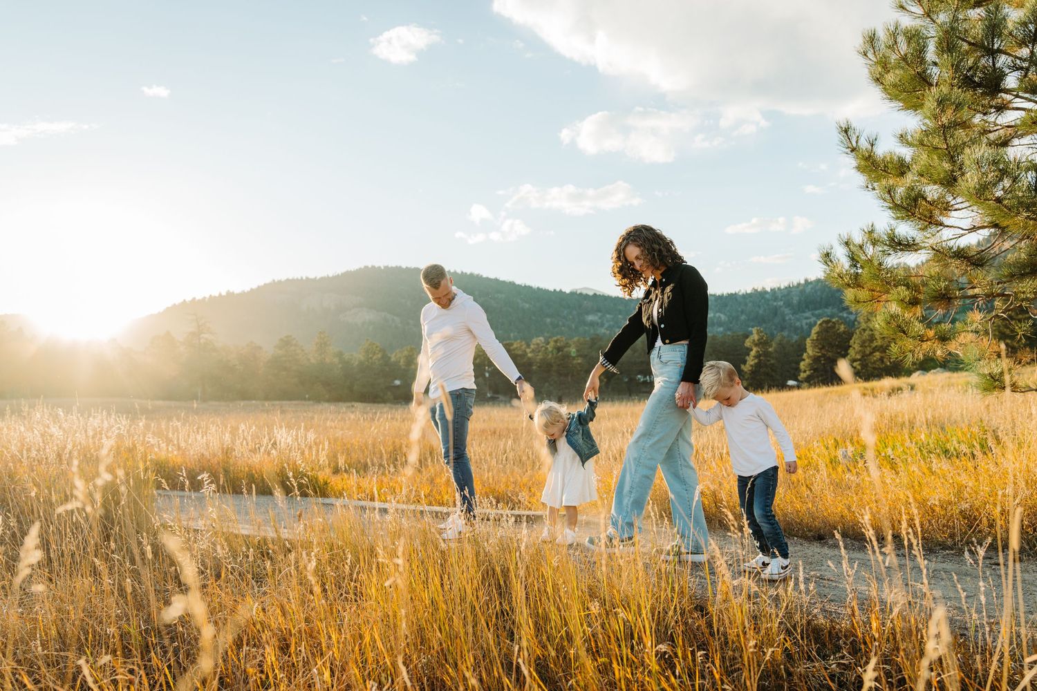 Family walking together through golden field at sunset with mountains in background.