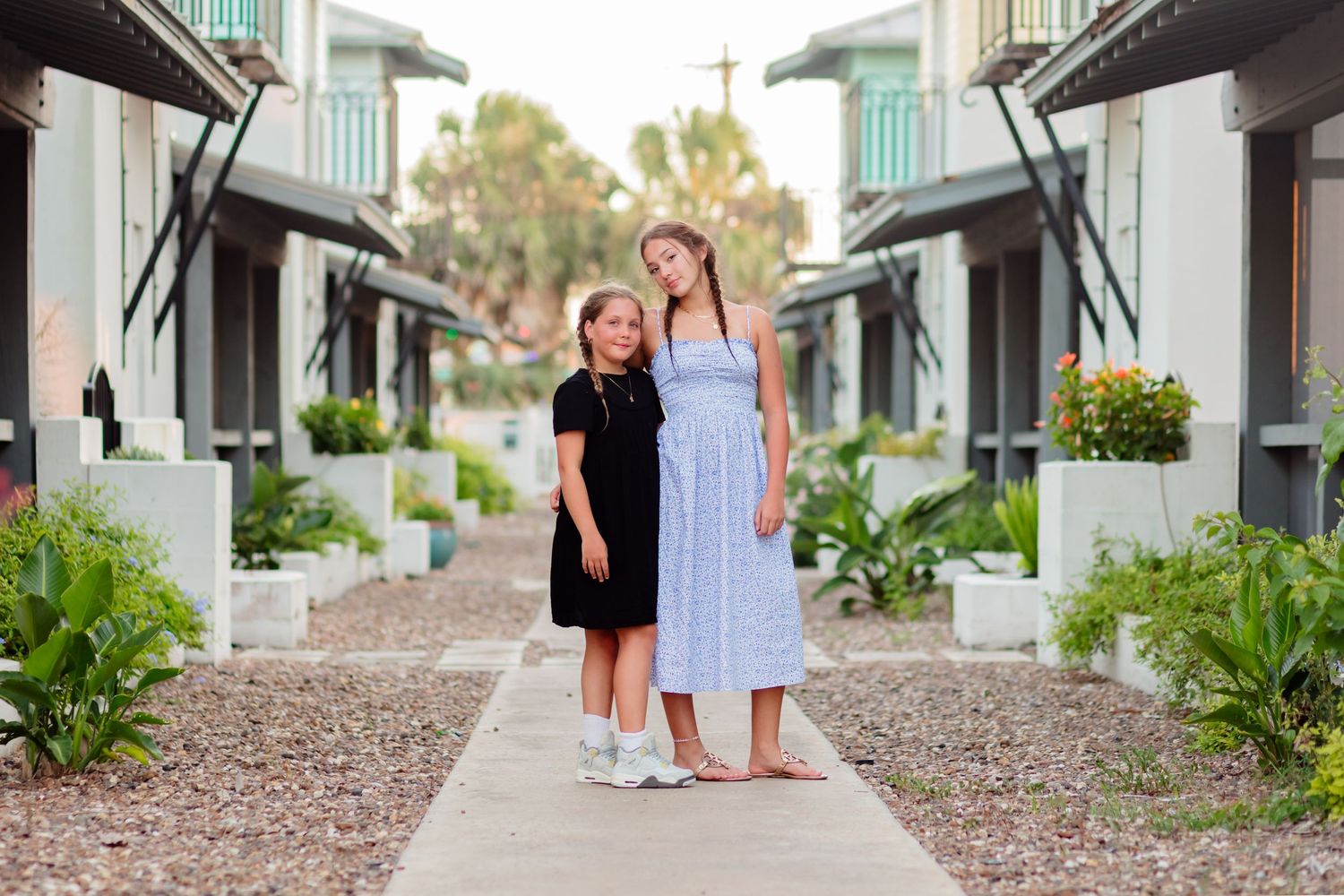 Two people in dresses stand together on a gravel path lined with coastal buildings and palm trees. Best Friend Beach Mini Port Aransas Texas