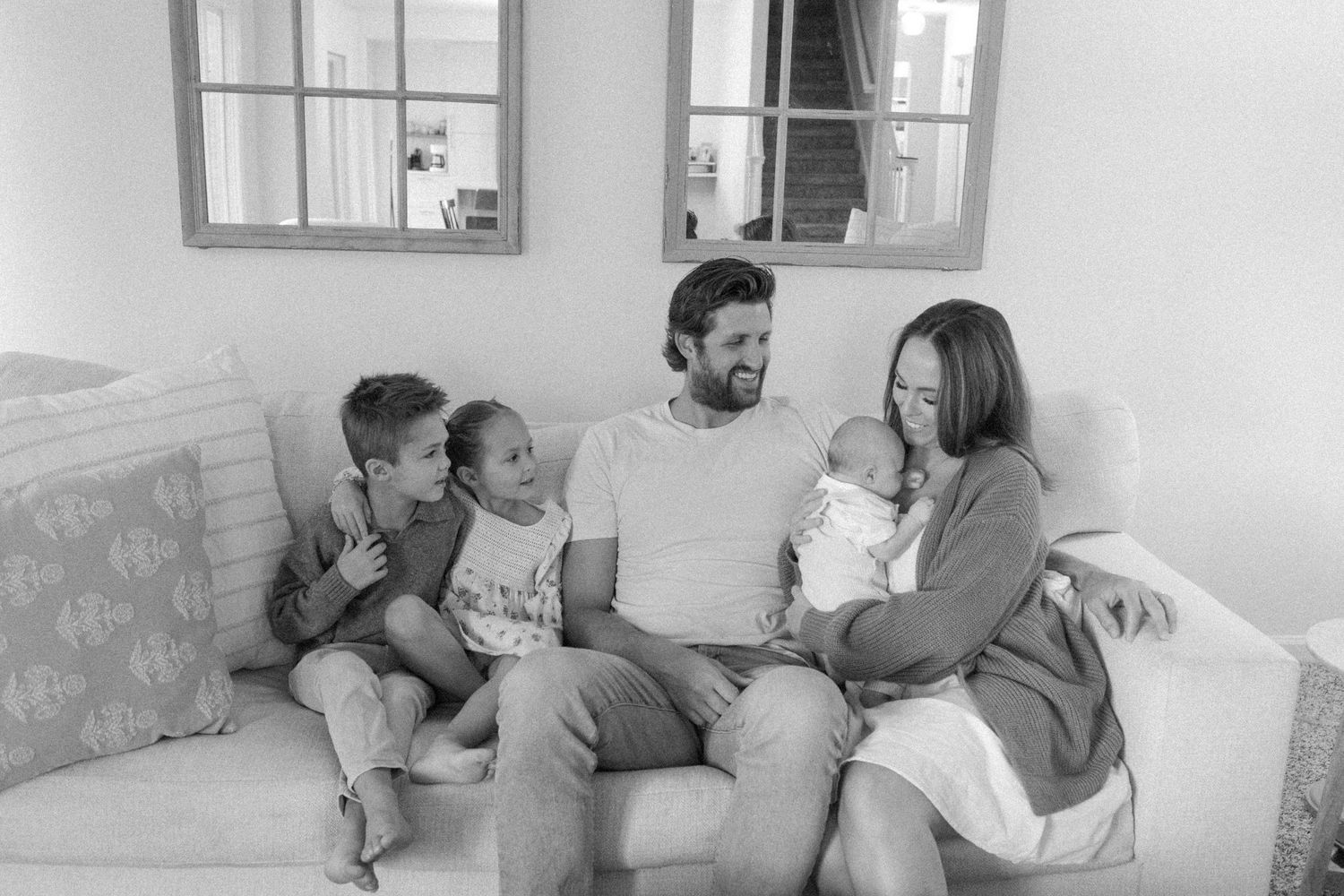 Black and white family portrait of parents with children relaxing on sofa.