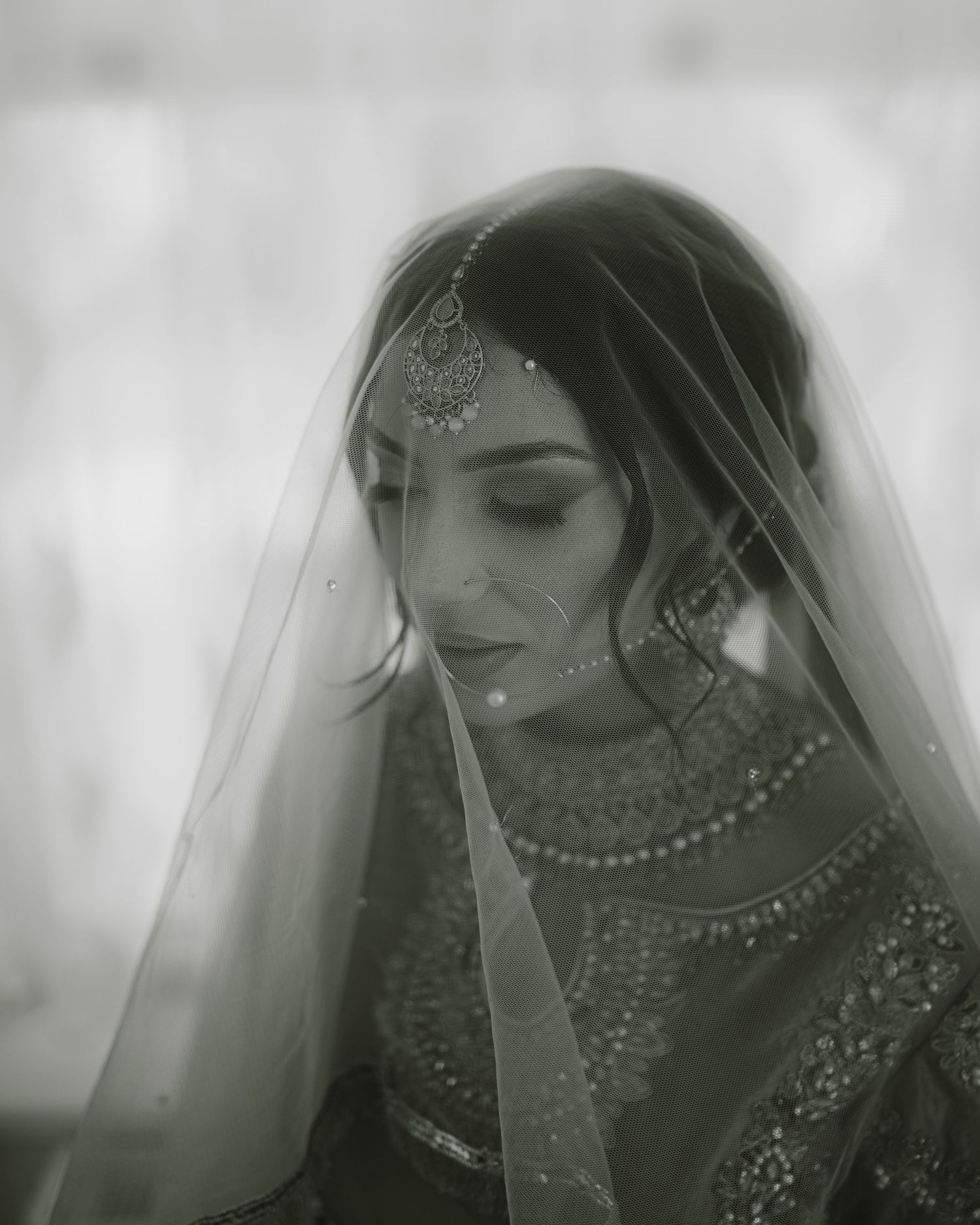 Black and white portrait showcasing ornate South Asian bridal jewelry and veil details.