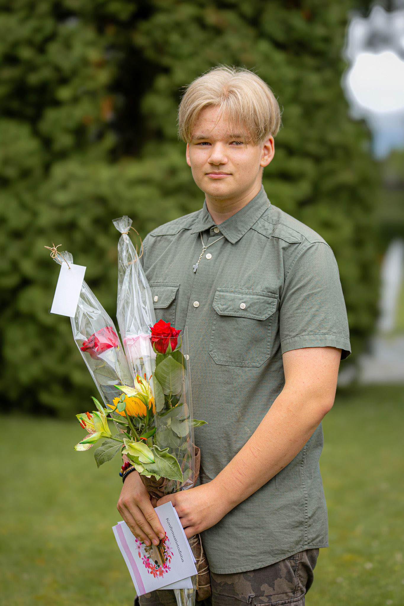 Nuori poika seisoo ulkona ja pitää kädessään kukkakimppuja ja kortteja.