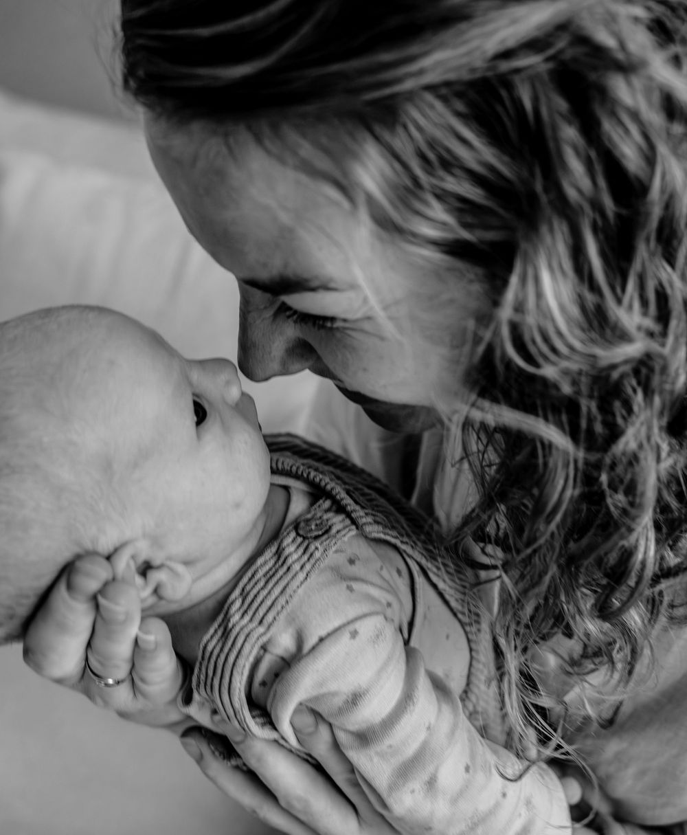 A tender black and white portrait showing an intimate moment between a parent and baby in close embrace.