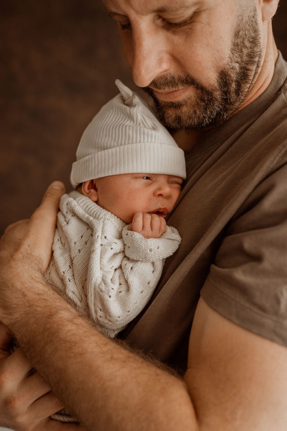 Close-up shots of a baby wearing a white knit hat being held lovingly against a brown background.