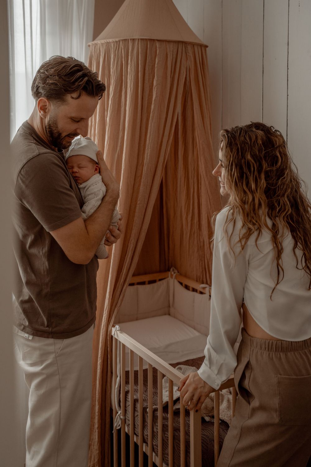 Lifestyle newborn photography session in a nursery with soft peachy curtains and natural lighting.