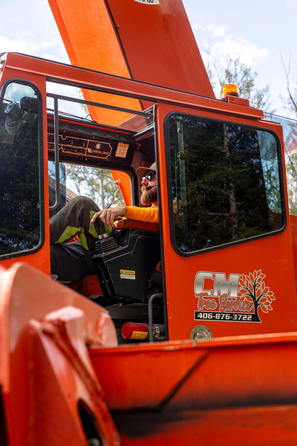 Orange tree service truck with worker visible through cab window.