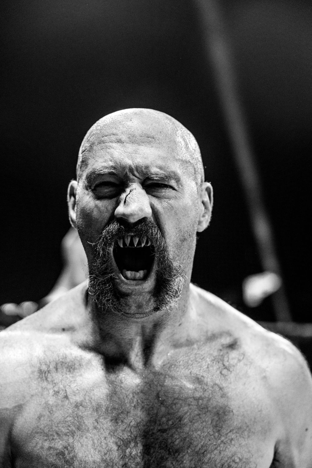 Black and white portrait of a muscular bald person screaming with an intense and aggressive facial expression.