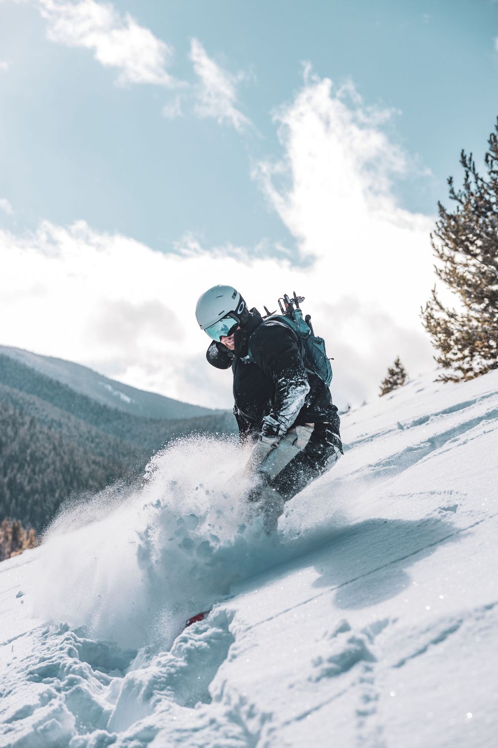 Snowboarder creating powder spray while riding down a snowy mountain slope.