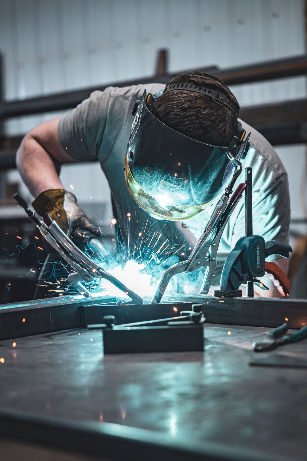Welder working on metal with bright blue welding sparks flying in industrial workshop.