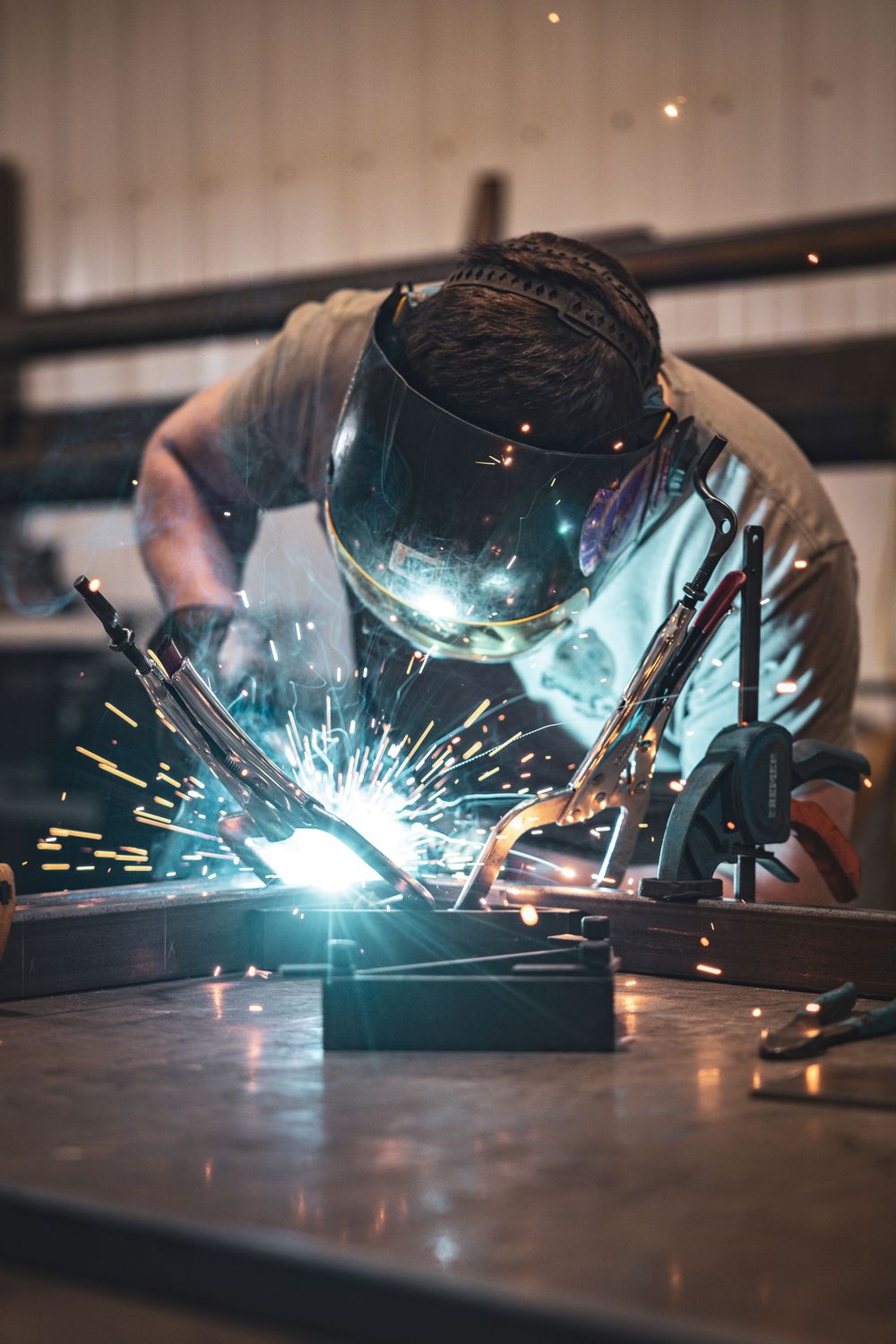 Close-up shot of welding process with bright blue sparks illuminating dark workshop space.