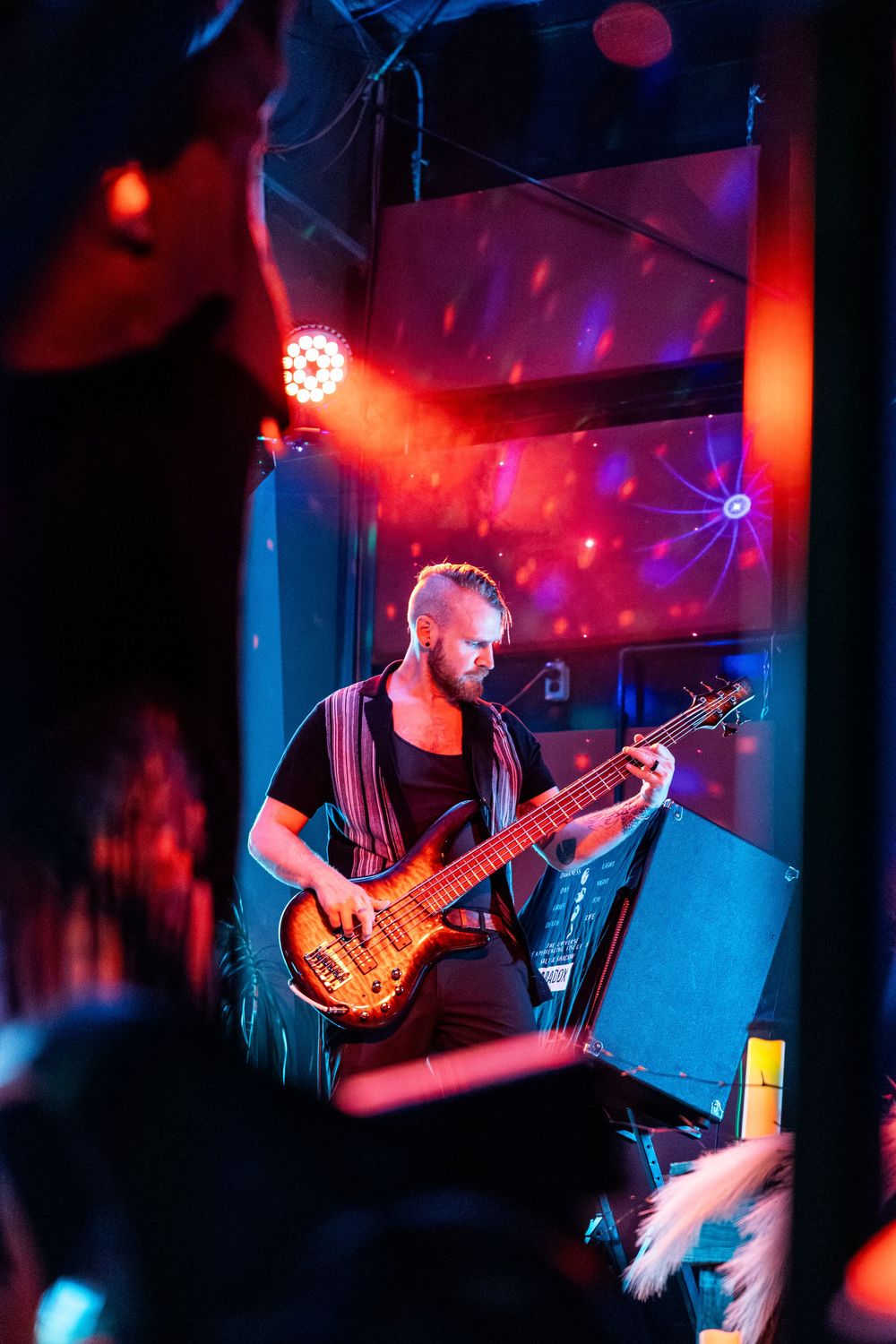 Male guitarist performing on stage under colorful red and blue lights at a live concert venue.