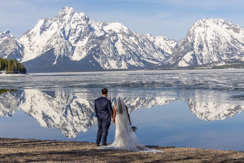 Scenic winter wedding photoshoot with snow-capped mountains and frozen lake creating a dramatic backdrop in Grand Teton National Park.