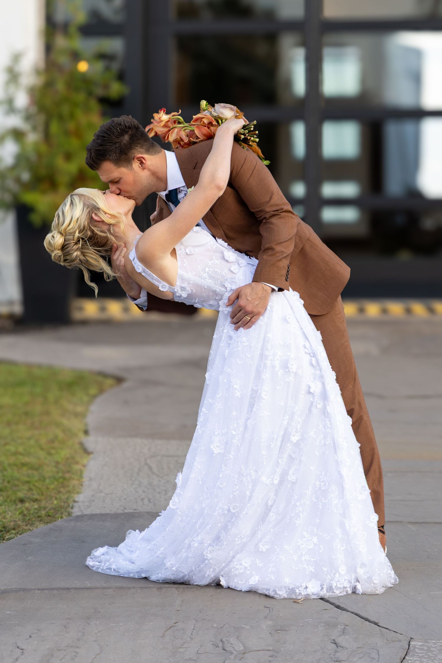 A couple in white dresses sharing an intimate moment under a blue draped arch.