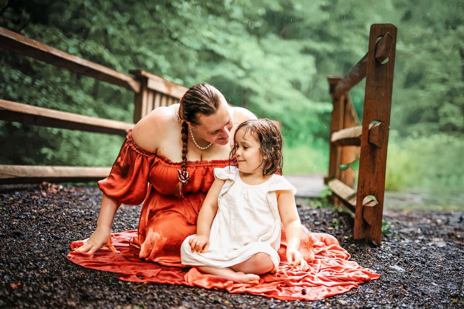 mother sitting outdoor in a pink gown in the rain loving on her physically impaired four year old daughter.