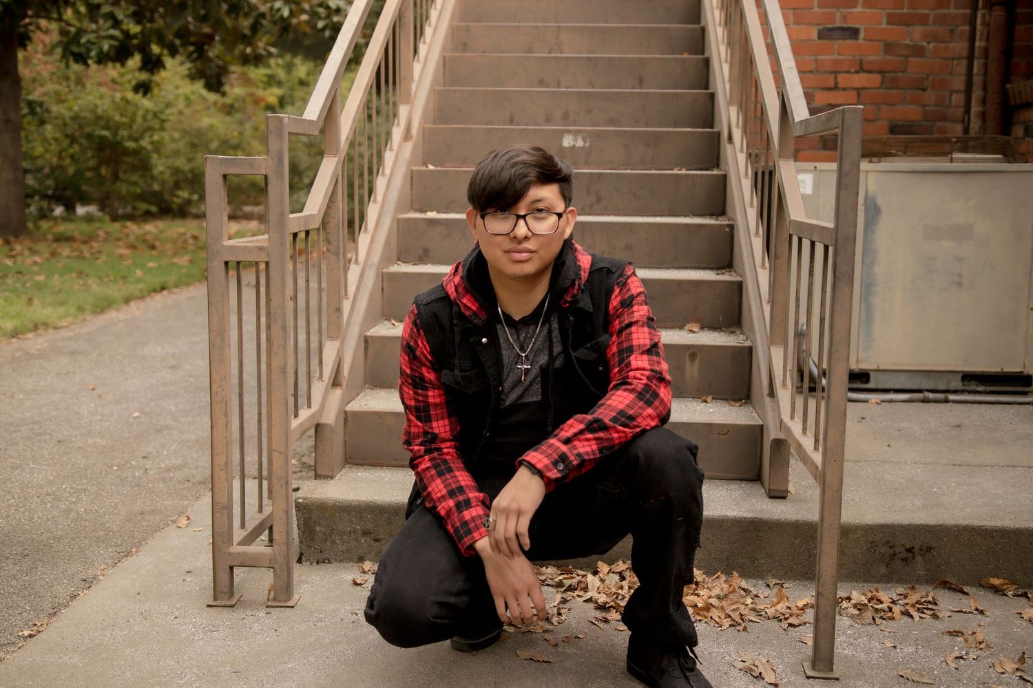 Someone in a red and black flannel shirt and black pants sits on outdoor concrete stairs.