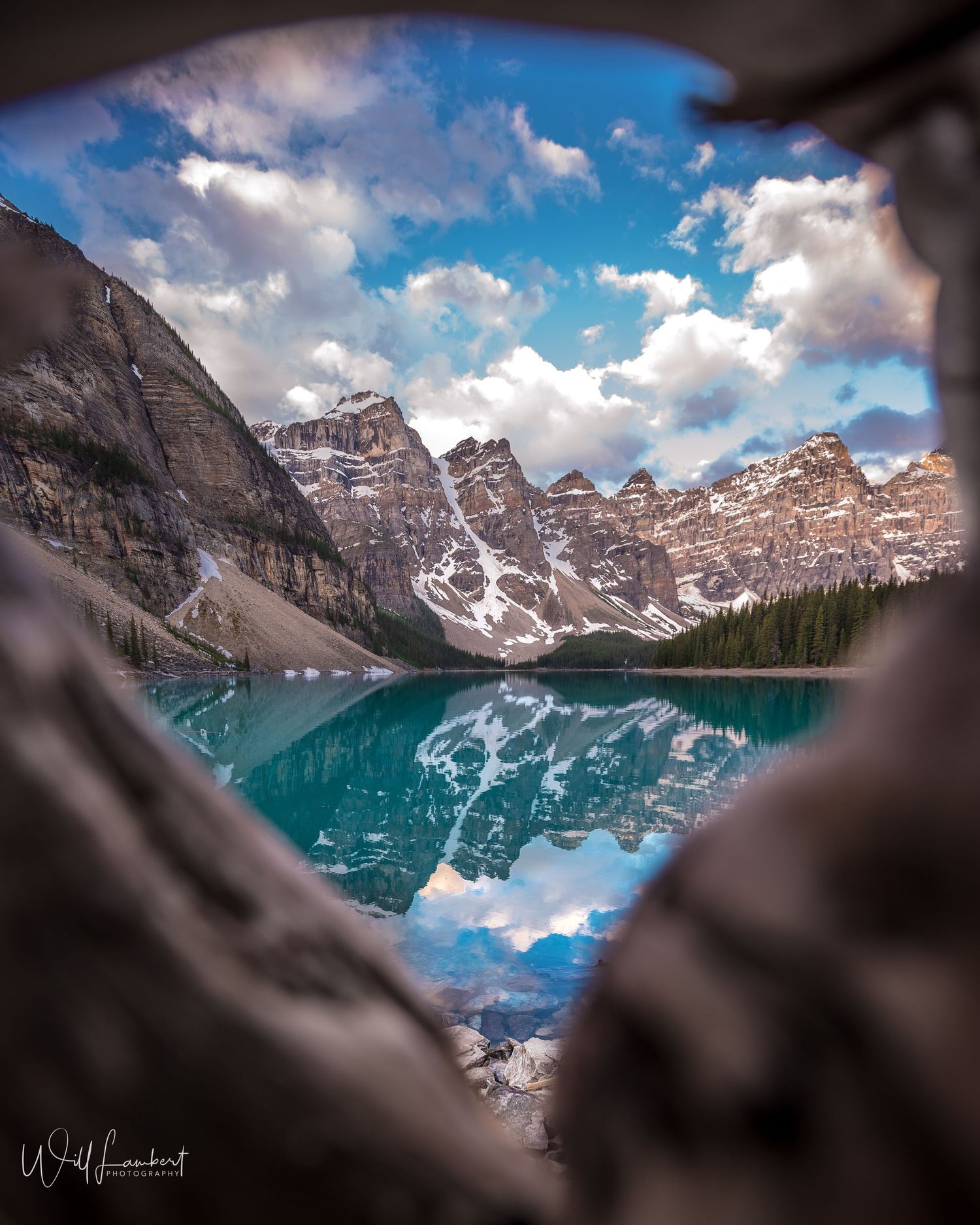 Framed view of Moraine Lake through rock formation with perfect mirror reflection of mountain peaks.