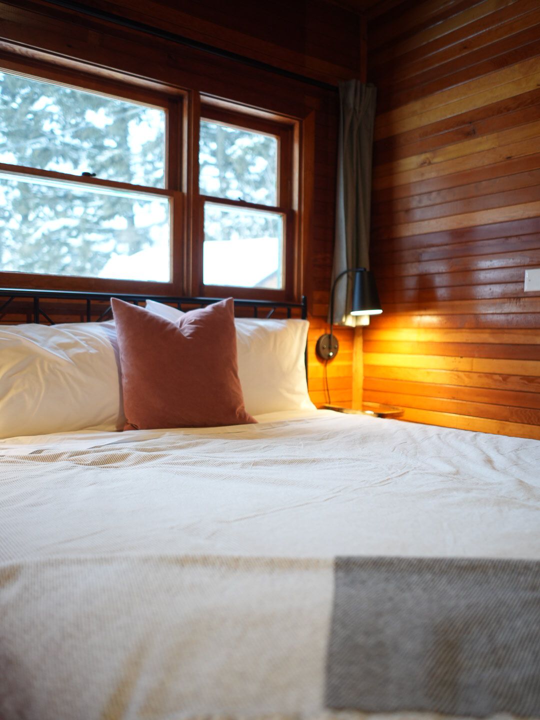 Modern cabin bedroom with wood paneling and large windows overlooking snowy landscape.