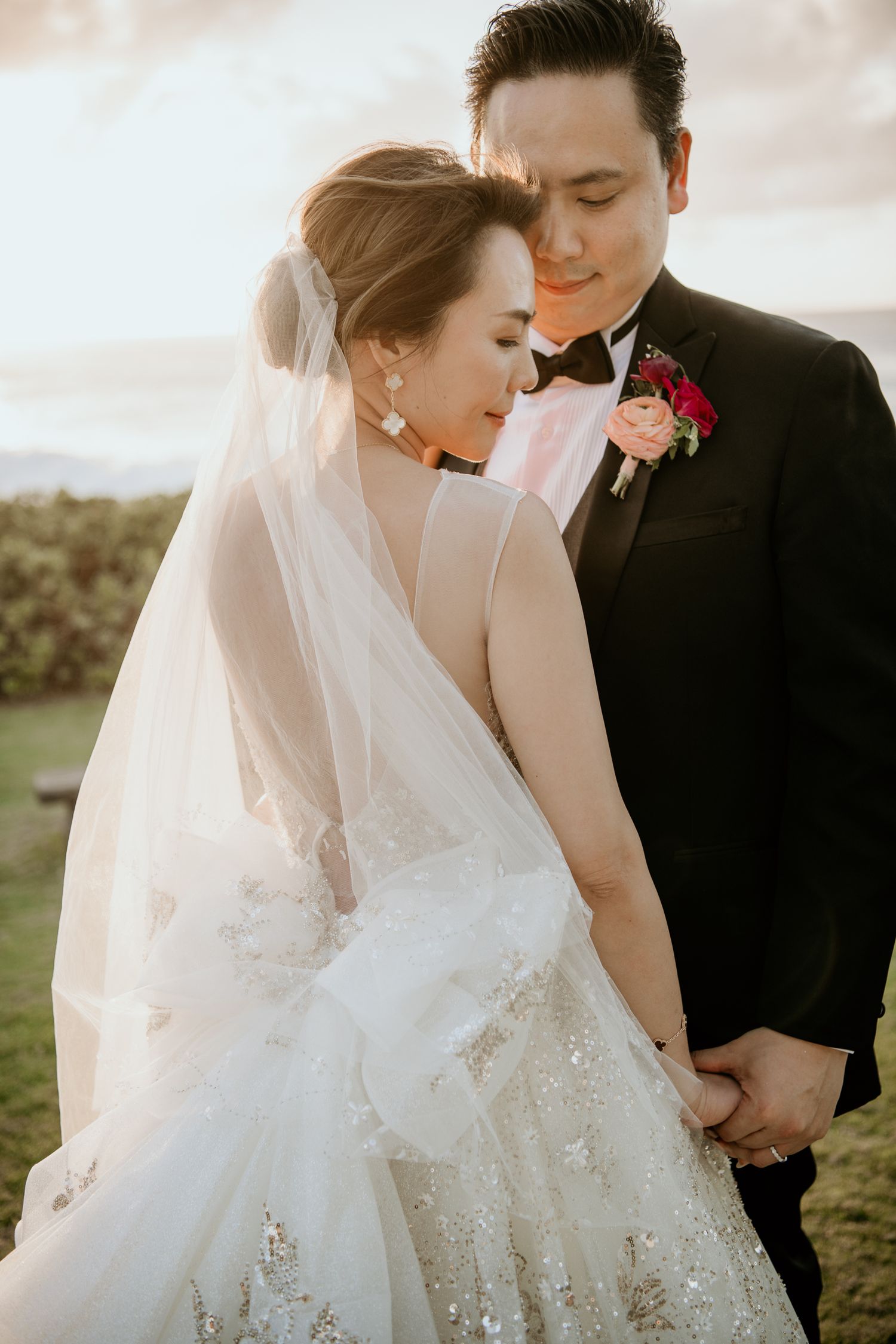 Intimate wedding photo showing newlyweds sharing tender moment in sunlit garden with bride in lace gown and flowing veil.
