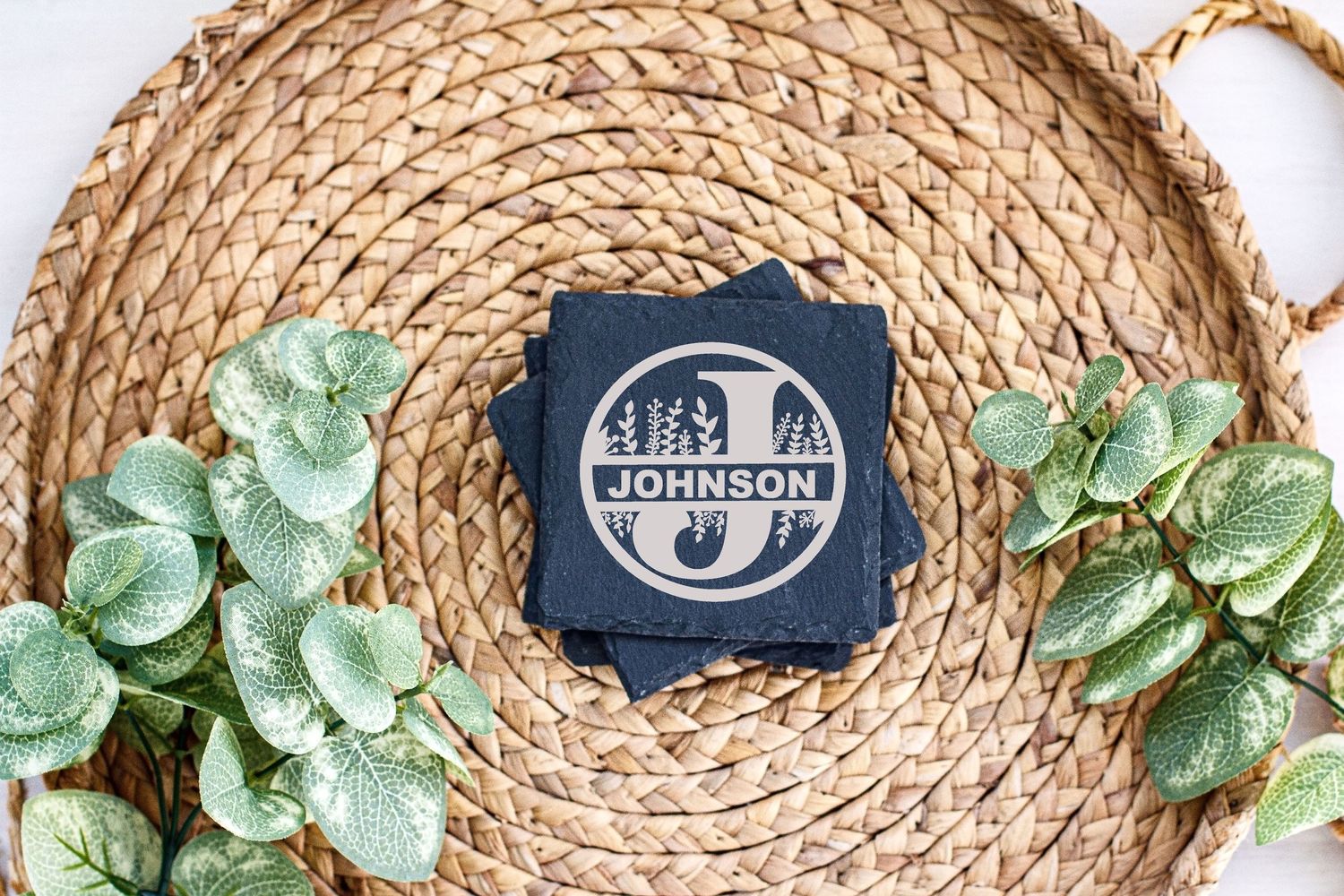 Monogram design on navy card displayed on circular woven placemat with decorative greenery.
