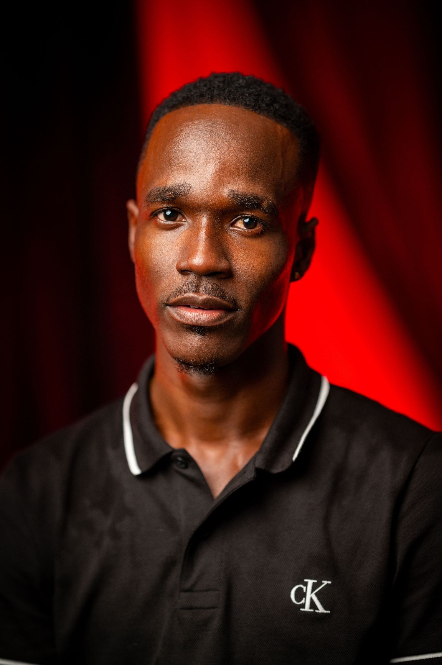 Professional headshot against red backdrop with dramatic lighting.