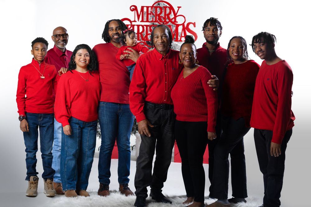 Family dressed in red sweaters posing together for a Merry Christmas holiday photo against a white background.