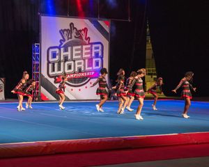 Cheerleaders perform routines at the Cheer World Championship competition on a blue mat under colorful stage lights.