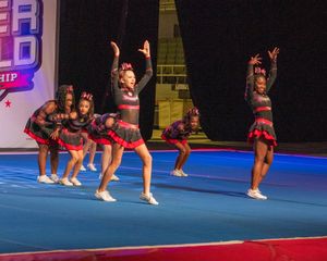 Young cheerleaders in red and black uniforms perform synchronized routine at competitive cheerleading championship event.