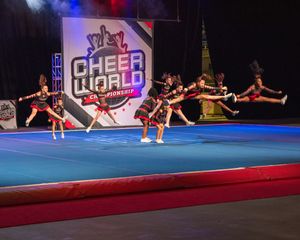 Cheerleaders performing stunts at Cheer World Championship competition on a blue mat under stage lights.
