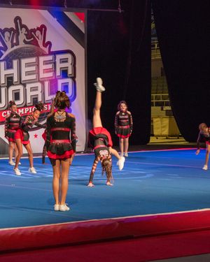 Cheerleaders perform stunts at Cheer World Championships on a blue mat, wearing red and black uniforms.