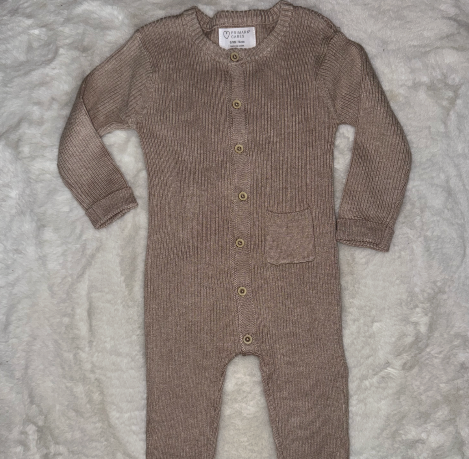Brown knit baby romper with buttons displayed on gray textured background.