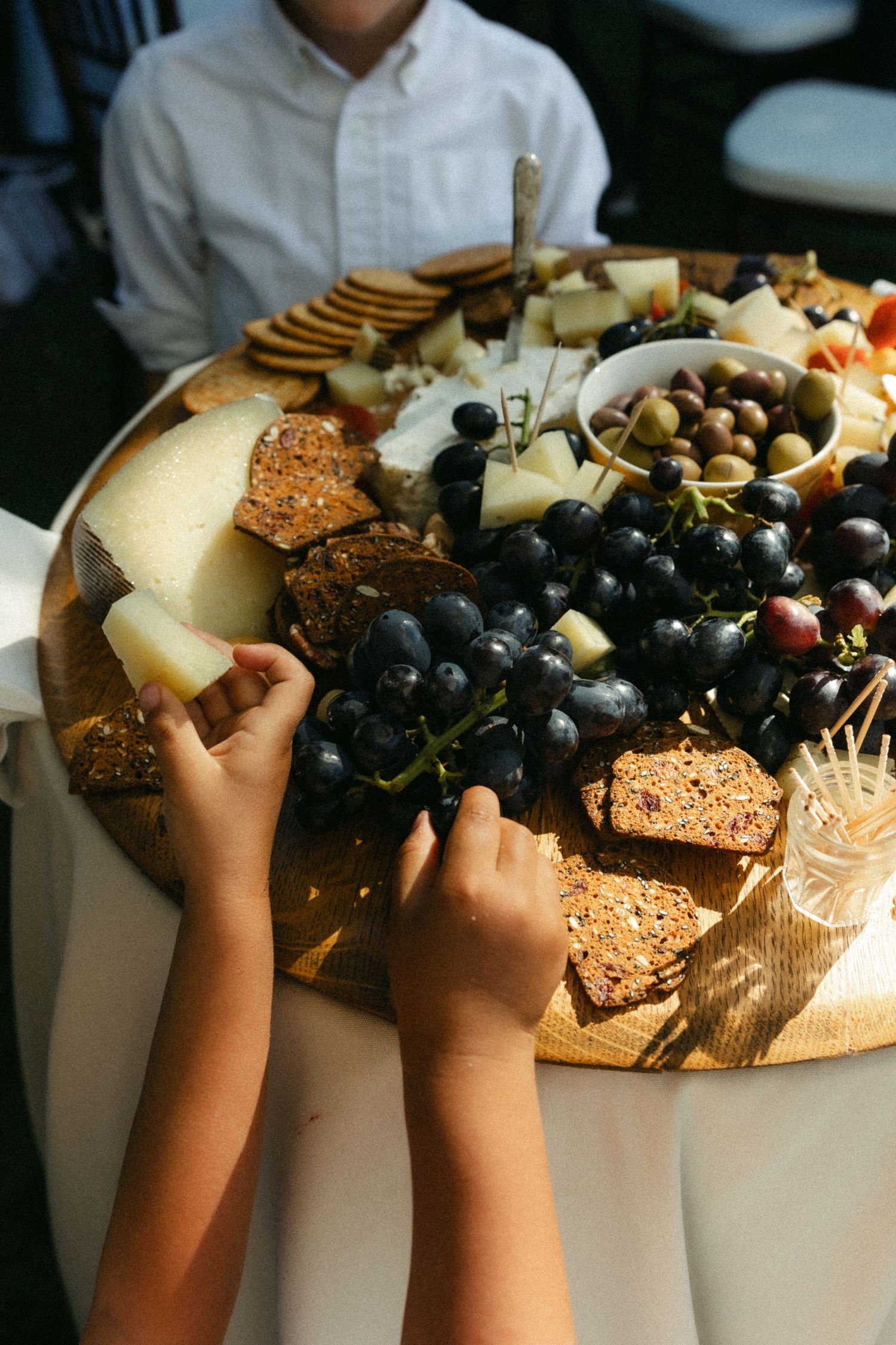 Hands reaching for cheese, crackers and grapes on an elegant charcuterie board.