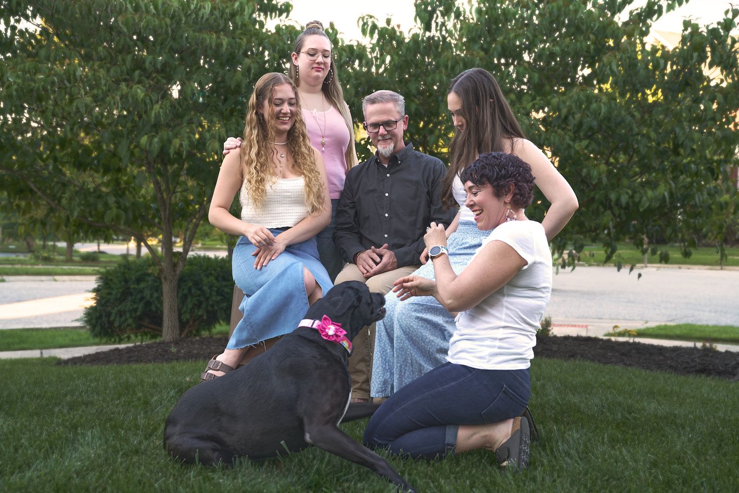 Parents and three teenage girls with mom playing with black dog