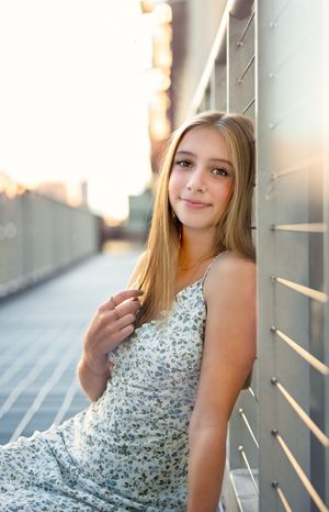 Portrait of a teen in a floral sundress leaning against a wall at sunset with soft golden lighting with a minneapolis senior photographer