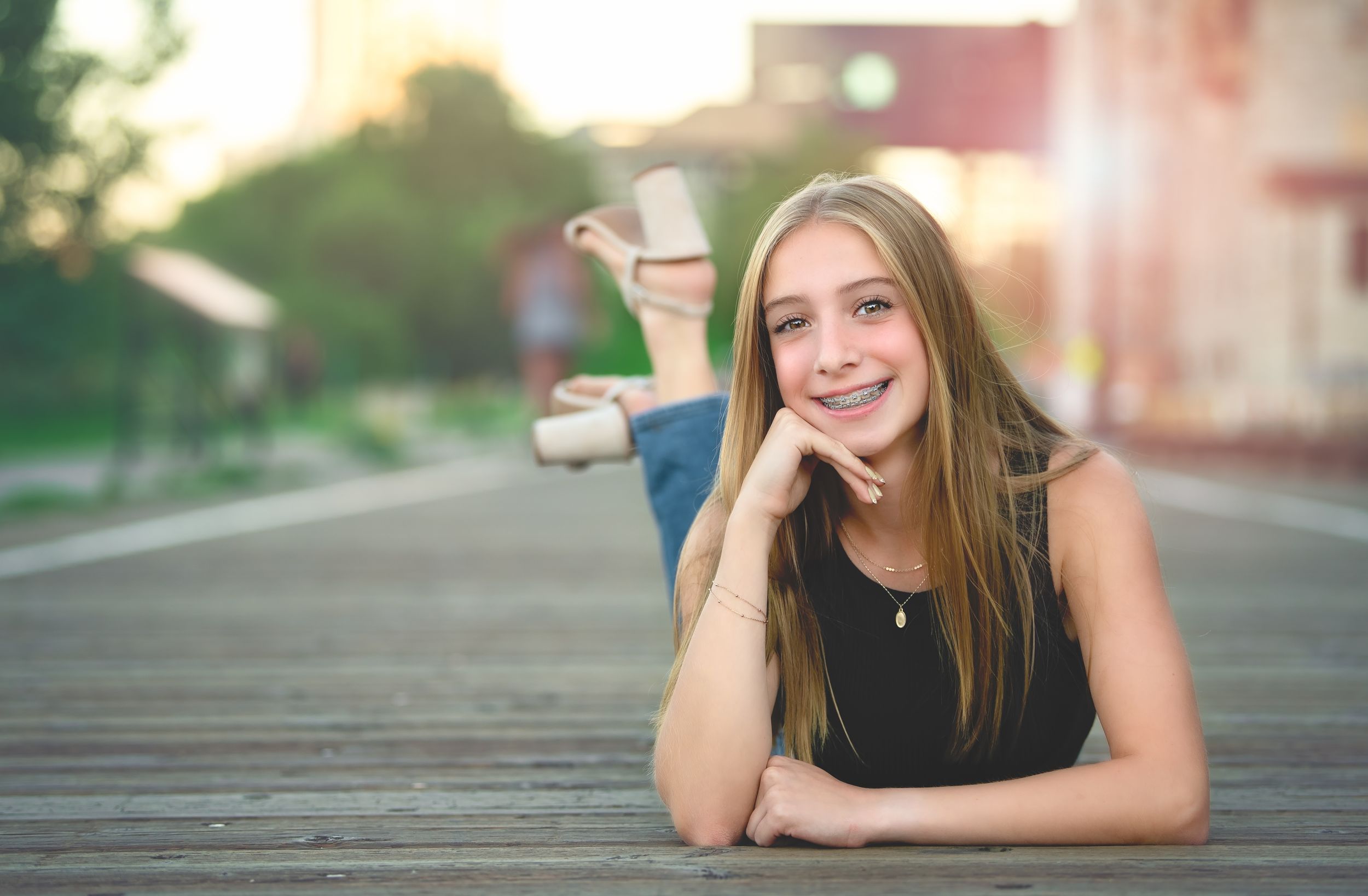 A person lying on a wooden boardwalk outdoors wearing a black sleeveless top on a sunny day for senior photos