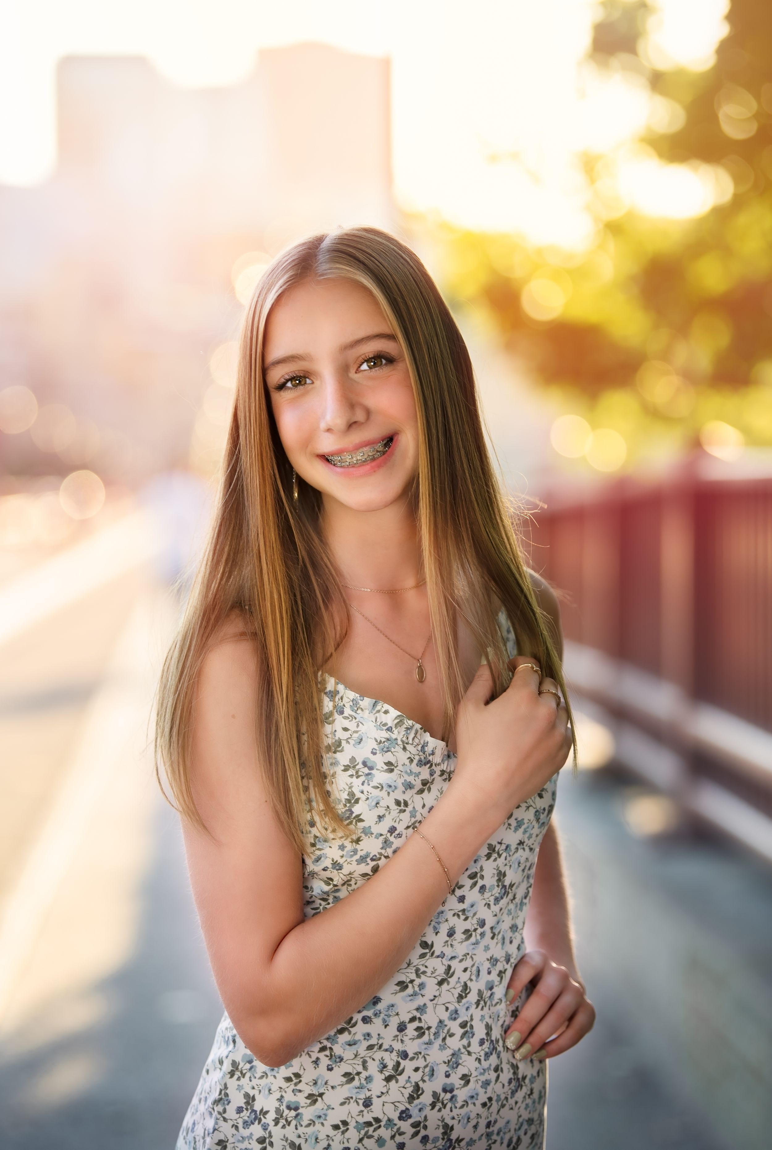 A teen in a floral sundress poses outdoors at sunset with golden bokeh lighting in the background for minneapolis senior photography