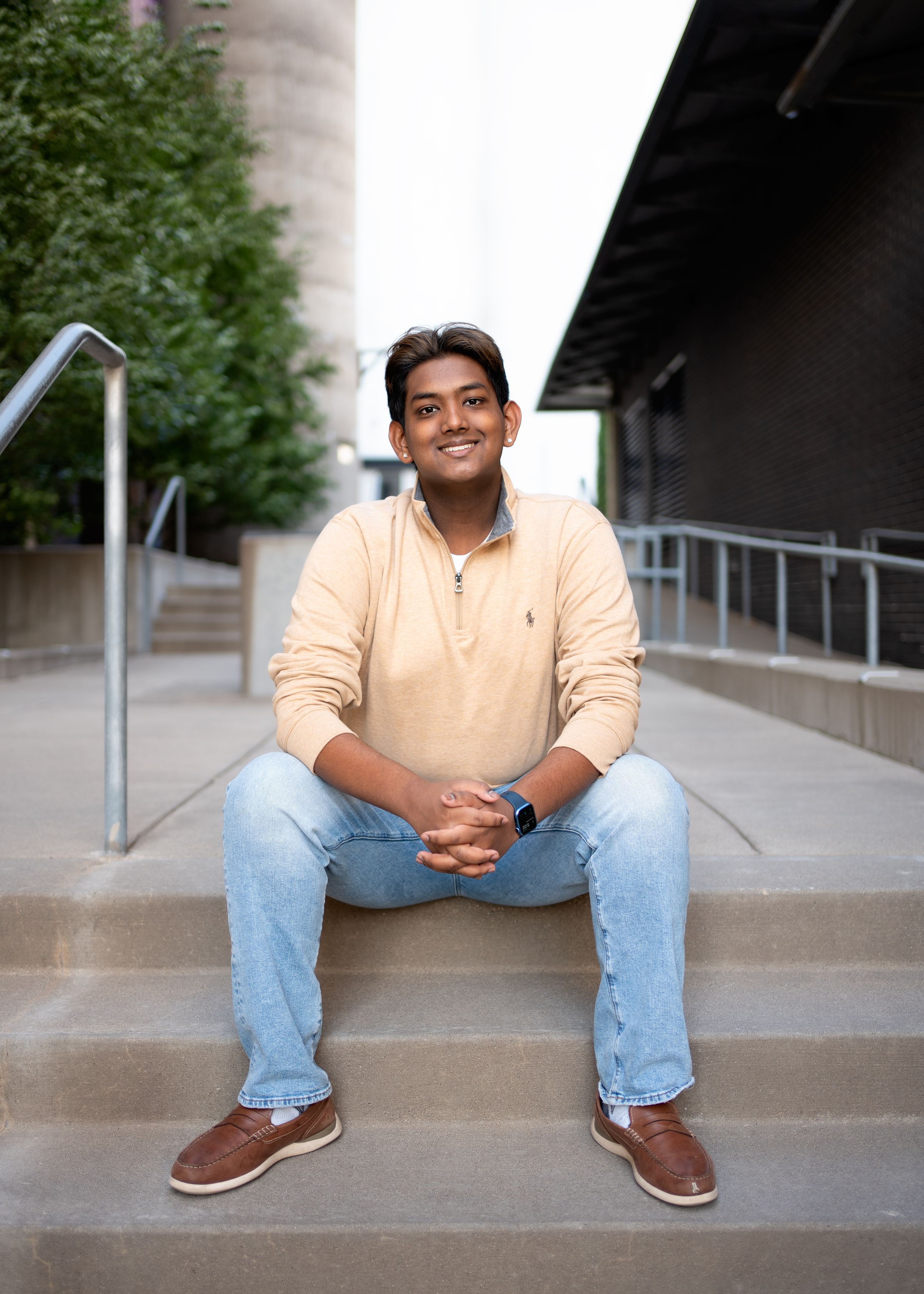 A person in a yellow sweater and jeans sits casually on concrete steps outside a building for minneapolis senior photography