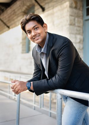 Young man in dark blazer and jeans leans casually on railing for senior photography in minneapolis