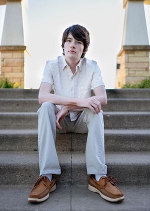 Young person in white shirt and khaki pants sits casually on concrete steps wearing brown boat shoes for minneapolis senior photography