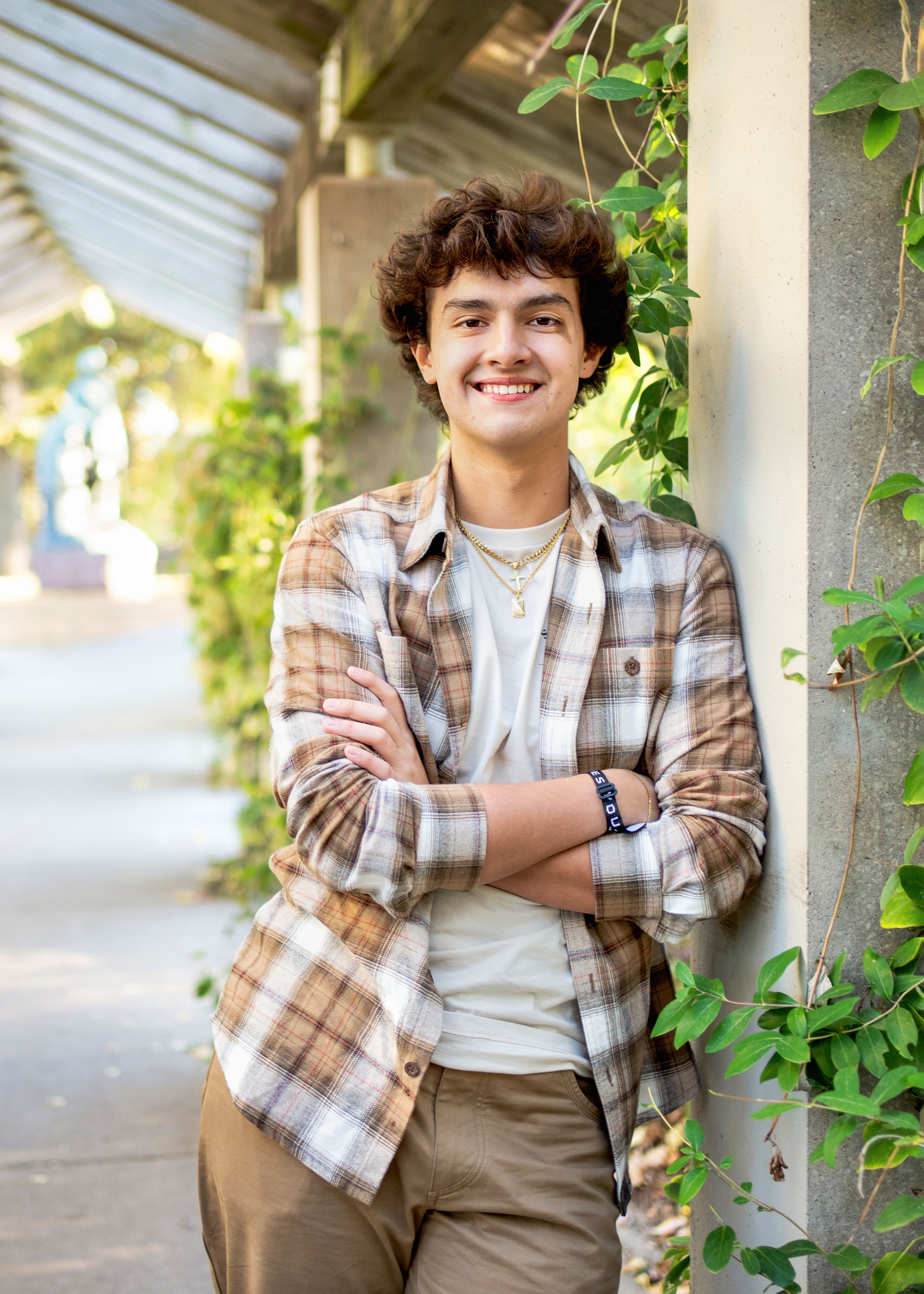 A teen wearing a plaid button-down shirt and khakis stands smiling with arms crossed for minneapolis senior photography