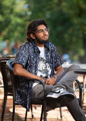 Person lounging in a patterned black button-down shirt and gray pants sits in a chair on sunny day during minneapolis senior photography